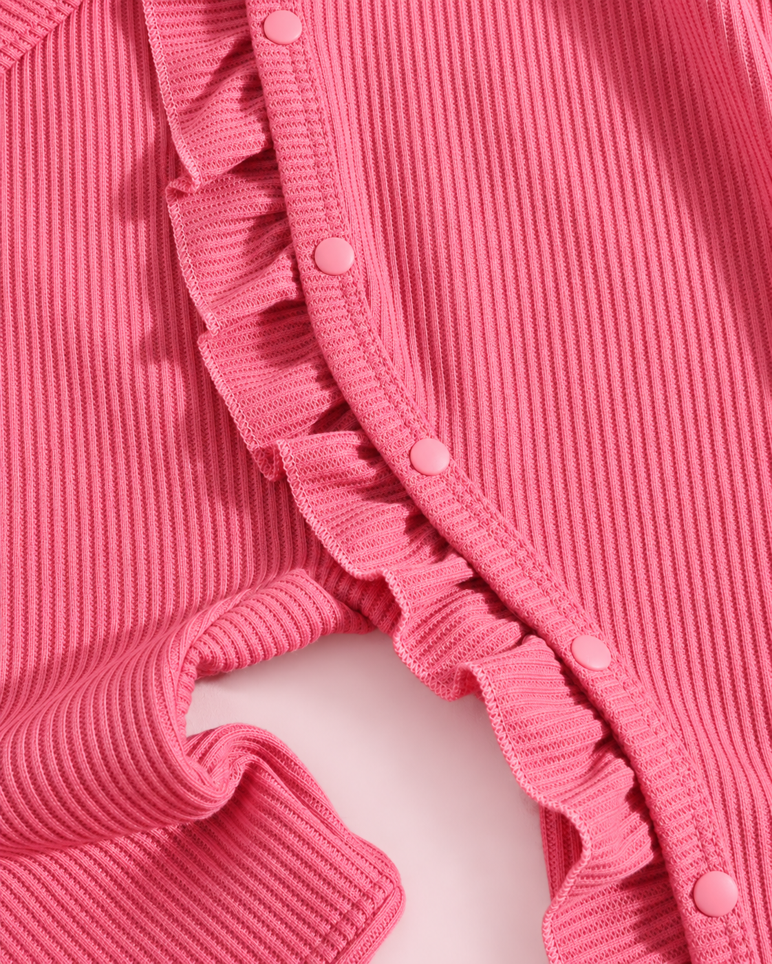 Curved snap fastening and ruffle detail on hot pink ribbed romper